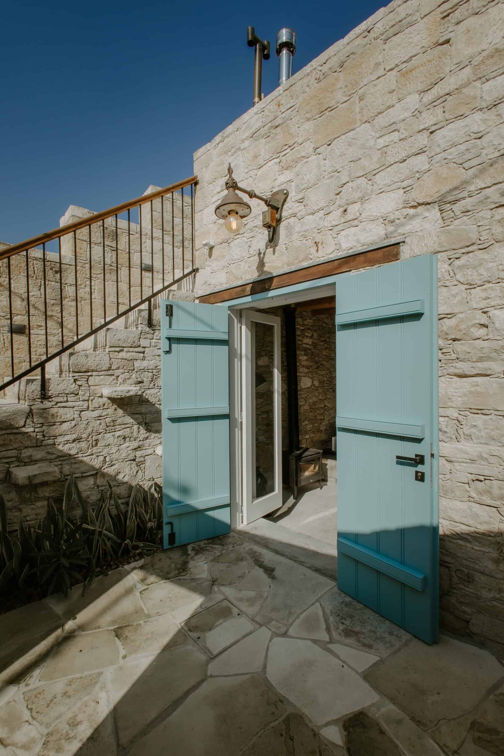Coastal stone building with open blue shutters, patio, and rustic exterior for interior design inspiration.