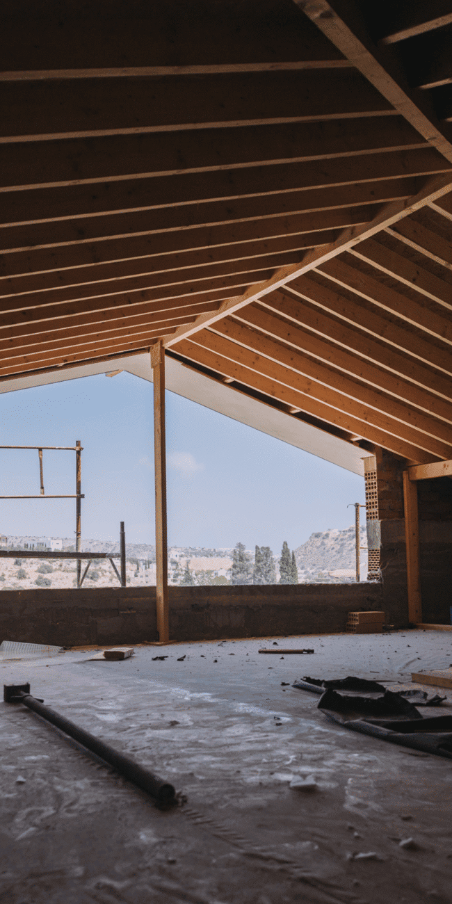 Modern home interior under construction with exposed wooden beams and scenic view outside.