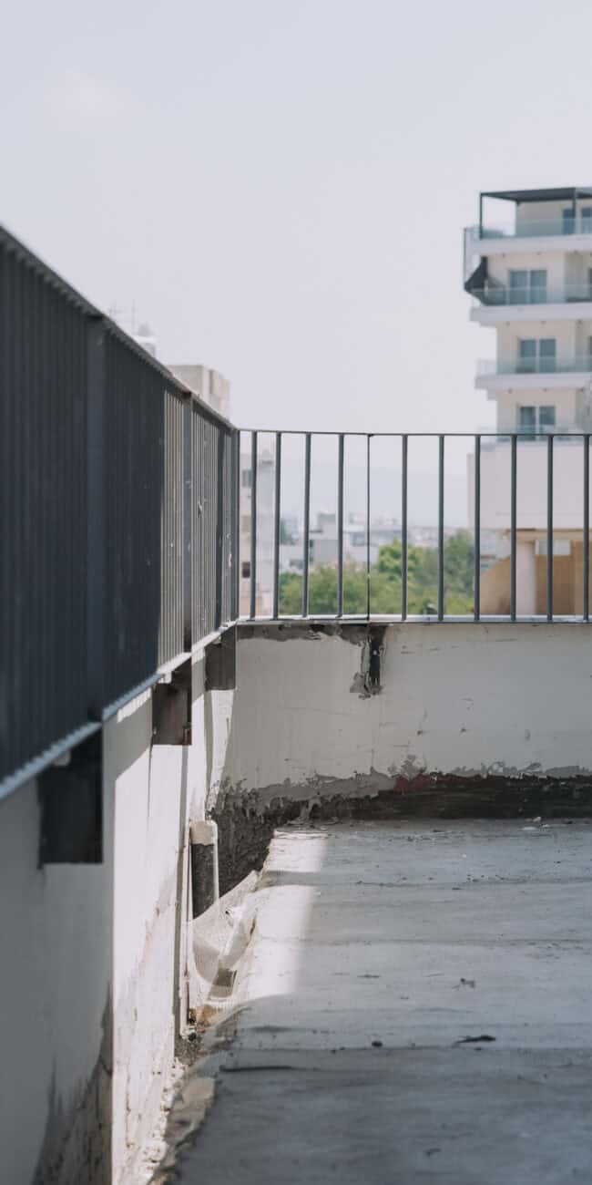 Empty balcony with metal railing and cityscape view, showcasing modern urban apartment interiors.