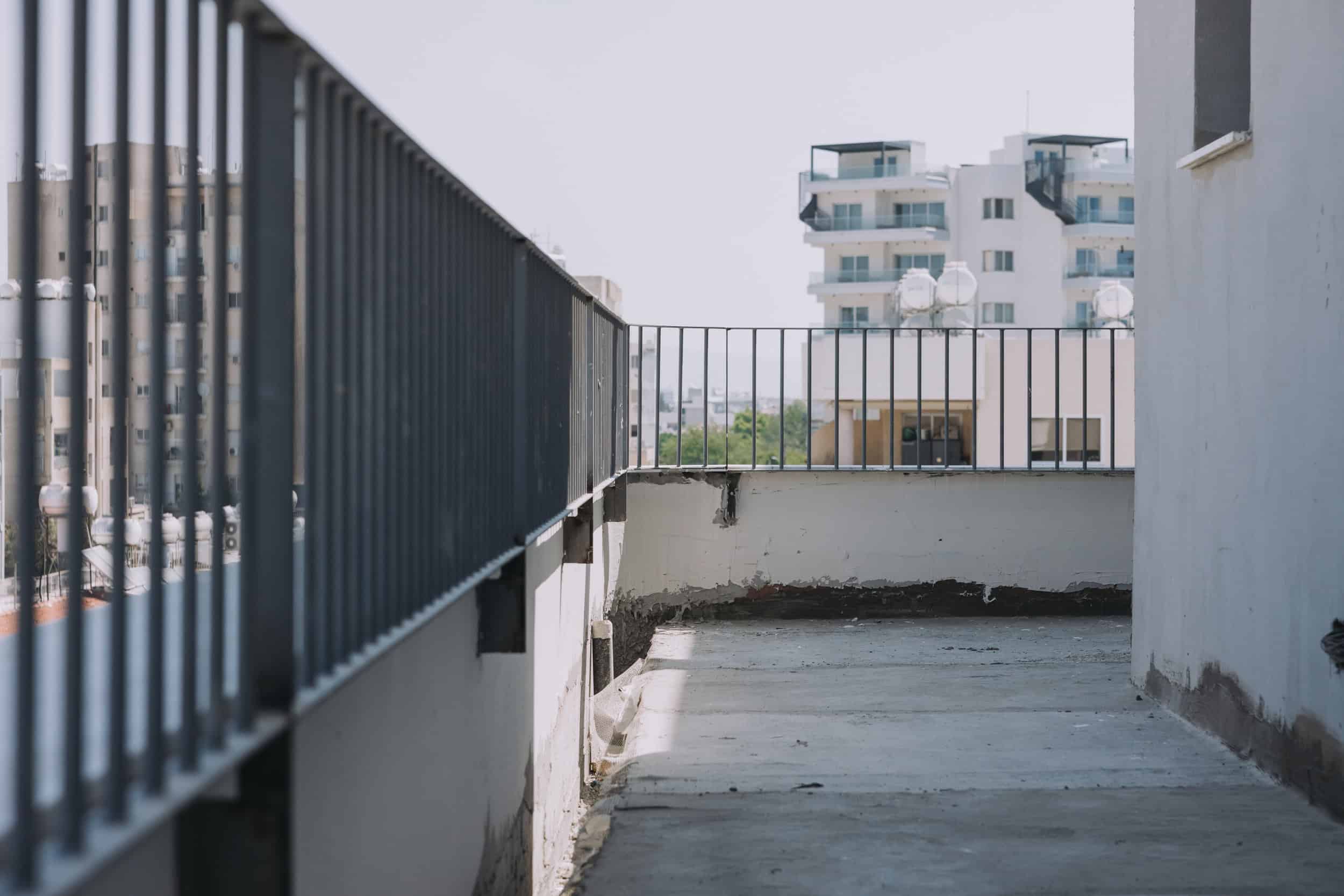 Empty balcony with metal railing and cityscape view, showcasing modern urban apartment interiors.